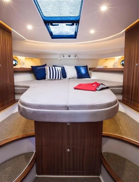 Interior of a yacht featuring a round bed with pillows, a skylight, and wooden finishes, creating a modern, nautical atmosphere.